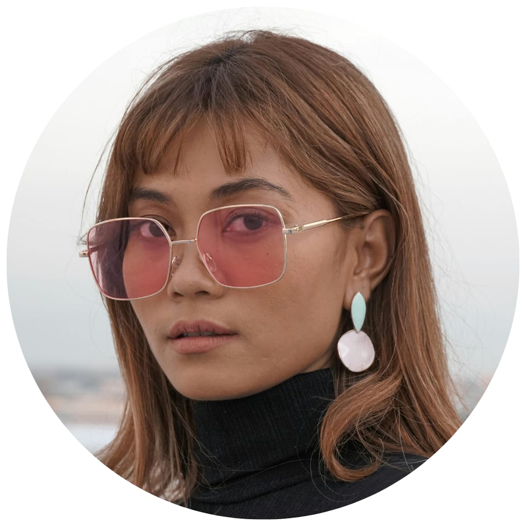 Woman with straight brown hair wearing pink sunglasses and pastel earrings."