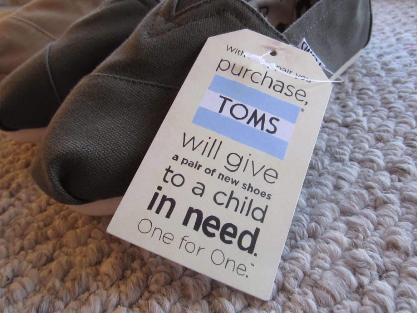 TOMS shoes with a tag that reads, ‘With every paid you purchase, TOMS will give a pair of new shoes to a child in need. One for One.’