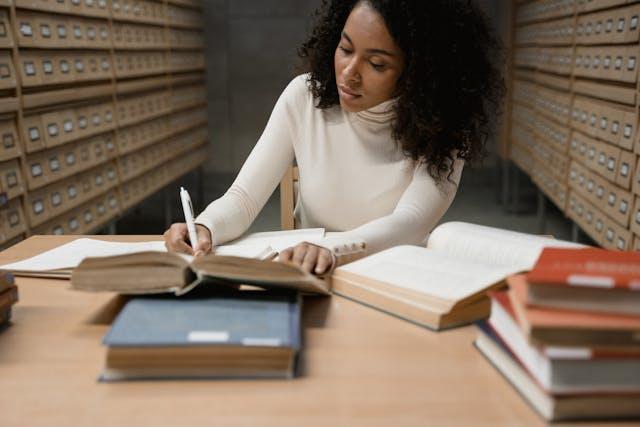 Woman writing in a library with open books on the table