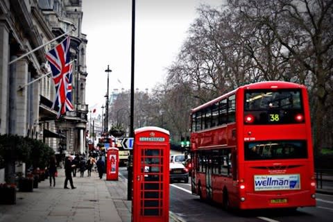 A street in England featuring a red phone booth and a red bus with a transit ad on the back